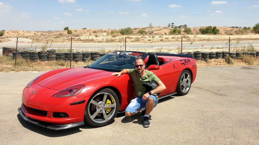 A customer kneeling in a helmet by the Corvette, the desert track behind