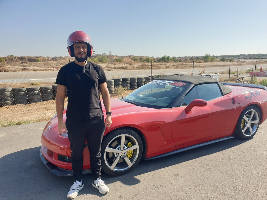 A customer in a helmet next to a red Corvette C6, on the track