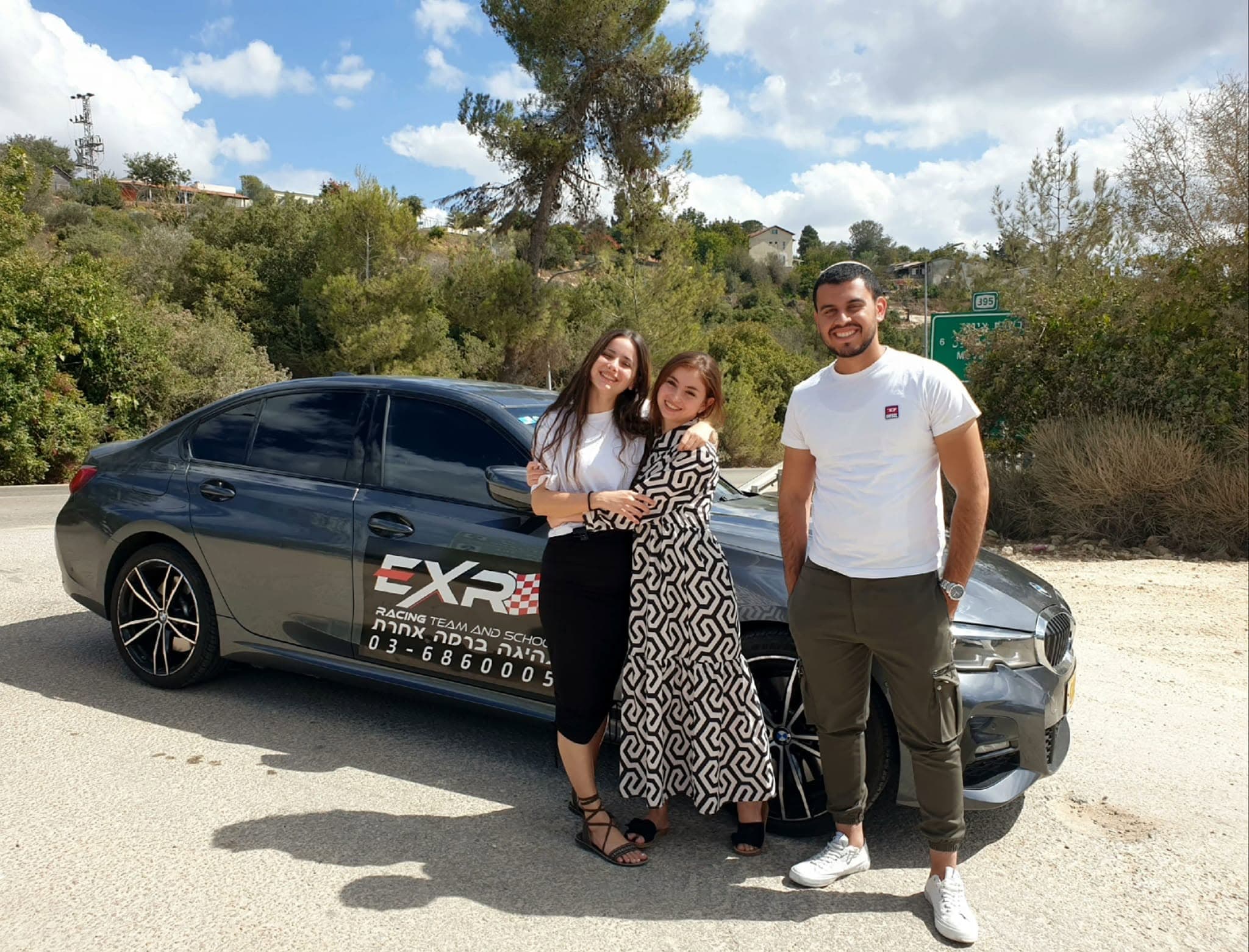 שלושה בני משפחה מחייכים ליד BMW של EXR בנוף הרי יהודה