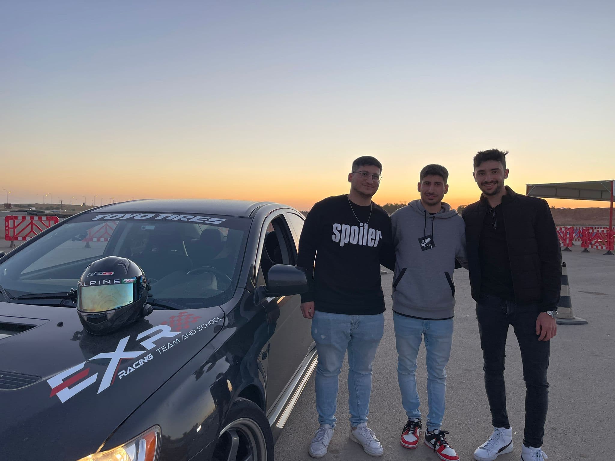 שלושה חברים מצטלמים ליד מיצובישי EVO X של EXR בשקיעה במסלול ערד